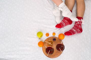 Image showing Soft photo of woman and man on the bed with tea and fruits, top view point. Female and male legs in warm woolen socks