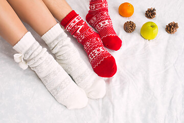 Image showing Soft photo of woman and man on the bed with phone and fruits, top view point. Female and male legs in warm woolen socks