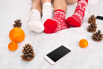 Image showing Soft photo of woman and man on the bed with phone and fruits, top view point. Female and male legs in warm woolen socks