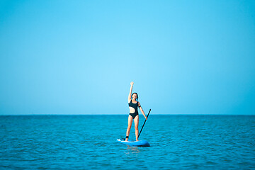 Image showing Happy beautiful young girl with paddle board on beach. Blue sea in the background. Summer vacation concept.