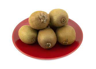 Image showing Whole kiwifruits with hairy skins piled on a red plate