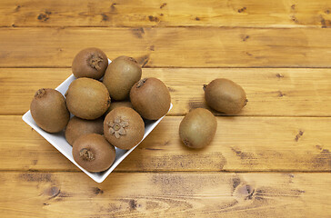 Image showing White bowl full of fresh kiwis, with spilled fruits