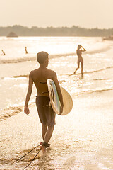 Image showing Man walking at tropical beach of Midigama, Sri Lankha at sunsen with surf board in his hands.
