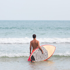 Image showing Rear view of unrecognizable male surfer at tropical beach with sup surf board and paddle in his hands