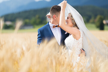 Image showing Groom hugs bride tenderly while wind blows her veil in wheat field somewhere in Slovenian countryside.