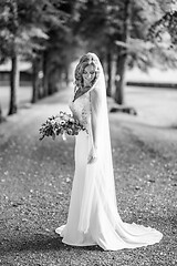 Image showing Full length portrait of beautiful sensual young blond bride in long white wedding dress and veil, holding bouquet outdoors in natural background.