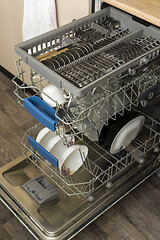 Image showing Clean plates, cups, spoons and forks in a dishwasher at home kitchen