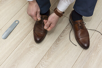 Image showing Hands of man in suit pants tying laces on classic shoes in everyday lifestyle