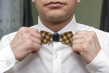 Image showing A man in white shirt straightens wooden bow tie in a rustic style