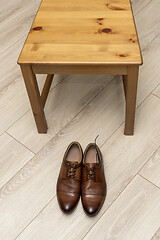 Image showing Classic men's shoes with laces near wooden chair on wooden floor, vertical