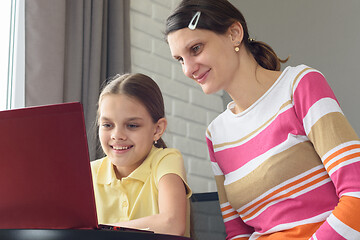 Image showing Happy girl and girl are sitting at the table and looking at the laptop screen.