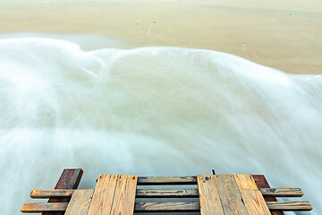 Image showing Waves roll onto a sandy beach, bottom part of a wooden bridge, long exposure