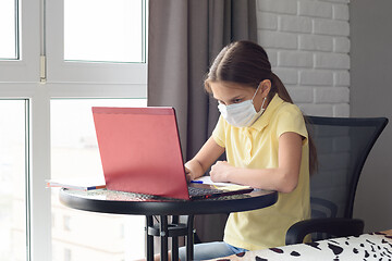 Image showing A girl in a medical mask learns remotely at home via the Internet