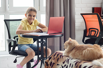 Image showing The girl looked in the frame doing homework online at home, on the bed lies a cat