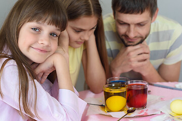 Image showing The family waits until the eggs are painted in a glass with dyes, the girl cheerfully looked into the frame