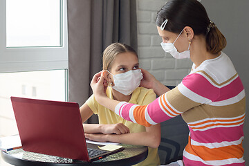 Image showing Mom puts on a girl a medical face mask while sitting in front of a computer at home
