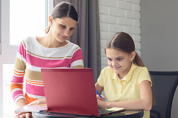 Image showing A girl and a girl are sitting at a table and browsing web pages in a laptop