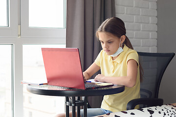 Image showing Pensive child sitting at the table taking off a medical mask and doing homework