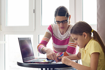 Image showing A home tutor teaches a child sitting at a table and using a computer
