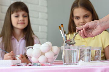 Image showing Mom pours vinegar in glasses of water for coloring eggs for Easter holidays