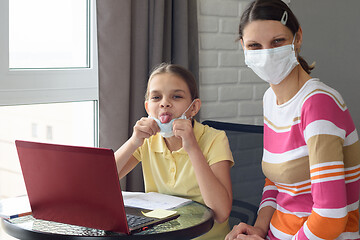 Image showing The girl took off her medical mask and showed her tongue, doing homework in self-isolation mode
