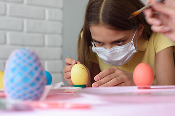 Image showing Close-up of a girl in a medical mask who paints Easter eggs