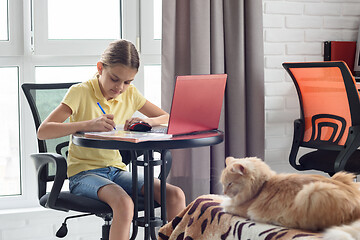 Image showing Girl sitting at a table in the room and doing homework online