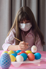 Image showing Sad quarantined girl paints Easter eggs with a brush