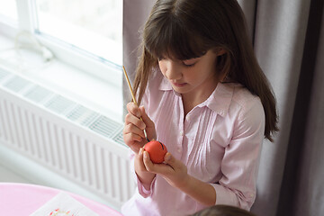 Image showing Girl paints an easter egg sitting by the window in a home environment