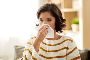 Image showing sick woman blowing nose in paper tissue at home