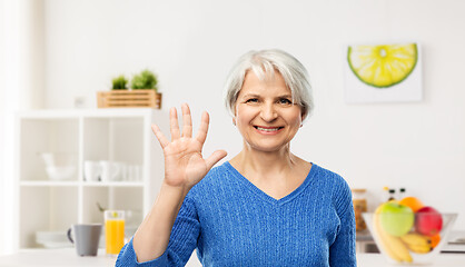 Image showing smiling senior woman showing her palm in kitchen