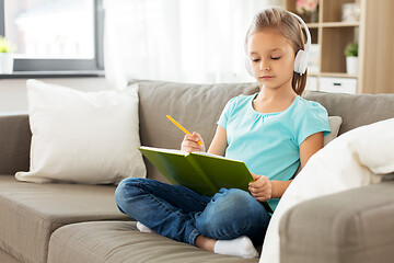 Image showing girl in headphones with diary on sofa at home