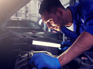 Image showing mechanic man with lamp repairing car at workshop