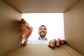 Image showing smiling man taking something out of parcel box