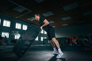 Image showing Shirtless man flipping heavy tire at gym