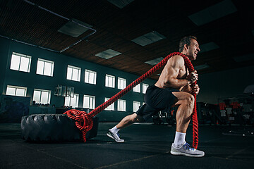 Image showing Shirtless man flipping heavy tire at gym