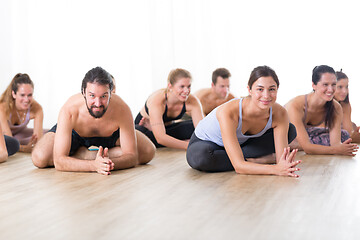 Image showing Group of young sporty attractive people in yoga studio, practicing yoga lesson with instructor, sitting on floor in forward band stretching yoga pose. Healthy active lifestyle, working out in gym