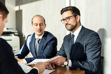 Image showing Group of confident successful business people reviewing and signing a contract to seal the deal at business meeting in modern corporate office.