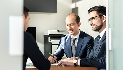 Image showing Group of confident successful business people reviewing and signing a contract to seal the deal at business meeting in modern corporate office.