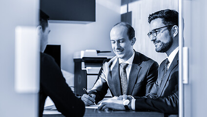Image showing Group of confident successful business people reviewing and signing a contract to seal the deal at business meeting in modern corporate office.