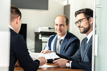 Image showing Group of confident successful business people reviewing and signing a contract to seal the deal at business meeting in modern corporate office.