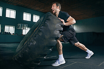 Image showing Shirtless man flipping heavy tire at gym