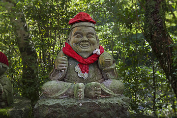 Image showing Old stone statue of Buddhist monk wearing knitted hat with fish in his hands.