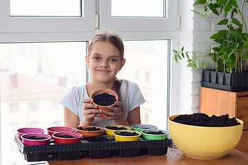 Image showing Cheerful girl holding a pot of land for planting plants and looked into the frame