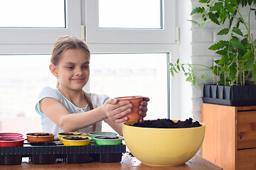 Image showing A girl poured earth for planting seeds in a pot of earth