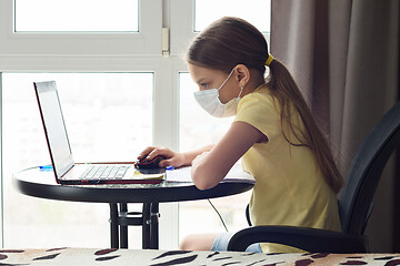 Image showing Girl in a medical mask watches an online lesson in a laptop