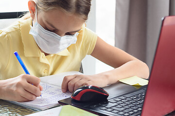 Image showing Portrait of a girl in a medical mask who learns lessons sitting at a table with a computer