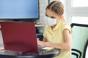 Image showing A girl in a medical protective mask undergoes distance learning