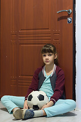 Image showing A girl with a ball sits at the door and is sad