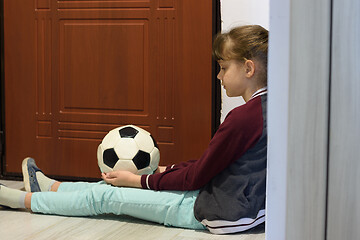 Image showing The quarantined girl in self-isolation sits with a ball at the front door